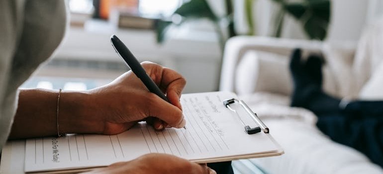 Woman writing on a clipboard while talking to her patient.