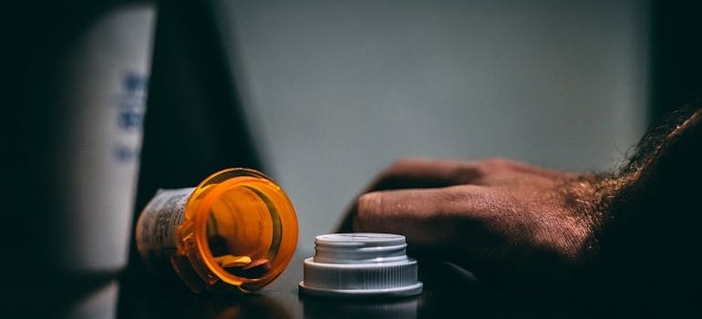 Man's hand next to a spilled bottle of pills.