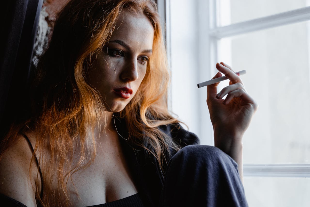 Woman sitting by the window and smoking a cigarette.