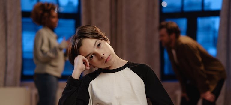 Boy sitting on a chair while his parents argue in the background.