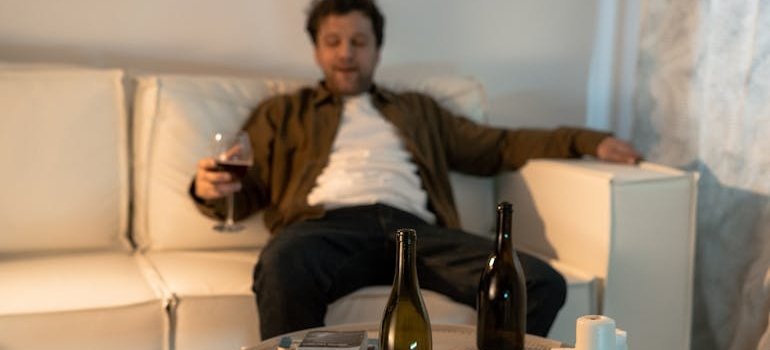 Man sitting on the couch drinking a glass of wine while struggling with PTSD and alcohol issues.