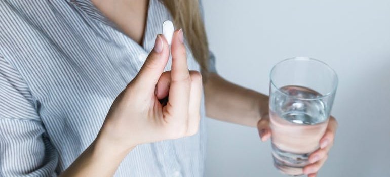 Woman holding a pill and a glass of water.