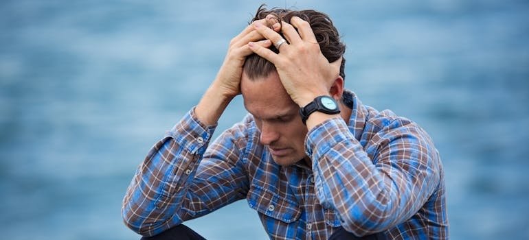 Man holding his head and worrying about socioeconomic status and addiction.