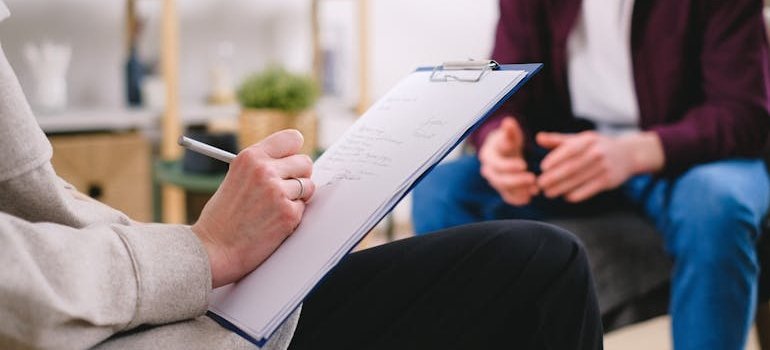 Woman writing in a clipboard while talking to a patient.