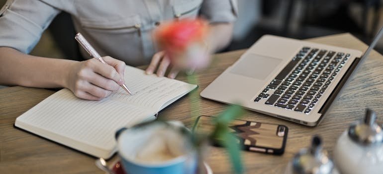 Woman writing in a notebook while looking at her laptop.