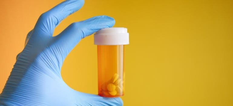Person wearing surgical gloves holding a bottle of prescription medication.