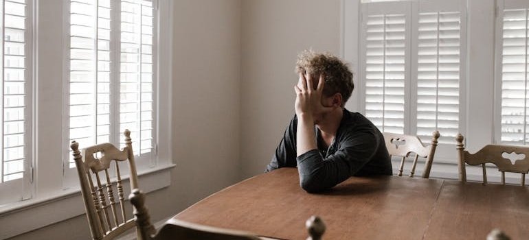 Man sitting at a kitchen table and worrying about a California sober lifestyle.