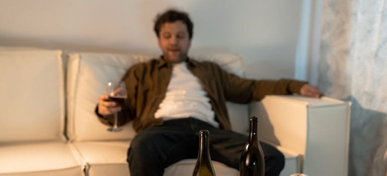 Man sitting on the couch, drinking a glass of wine and going through the stages of relapse.
