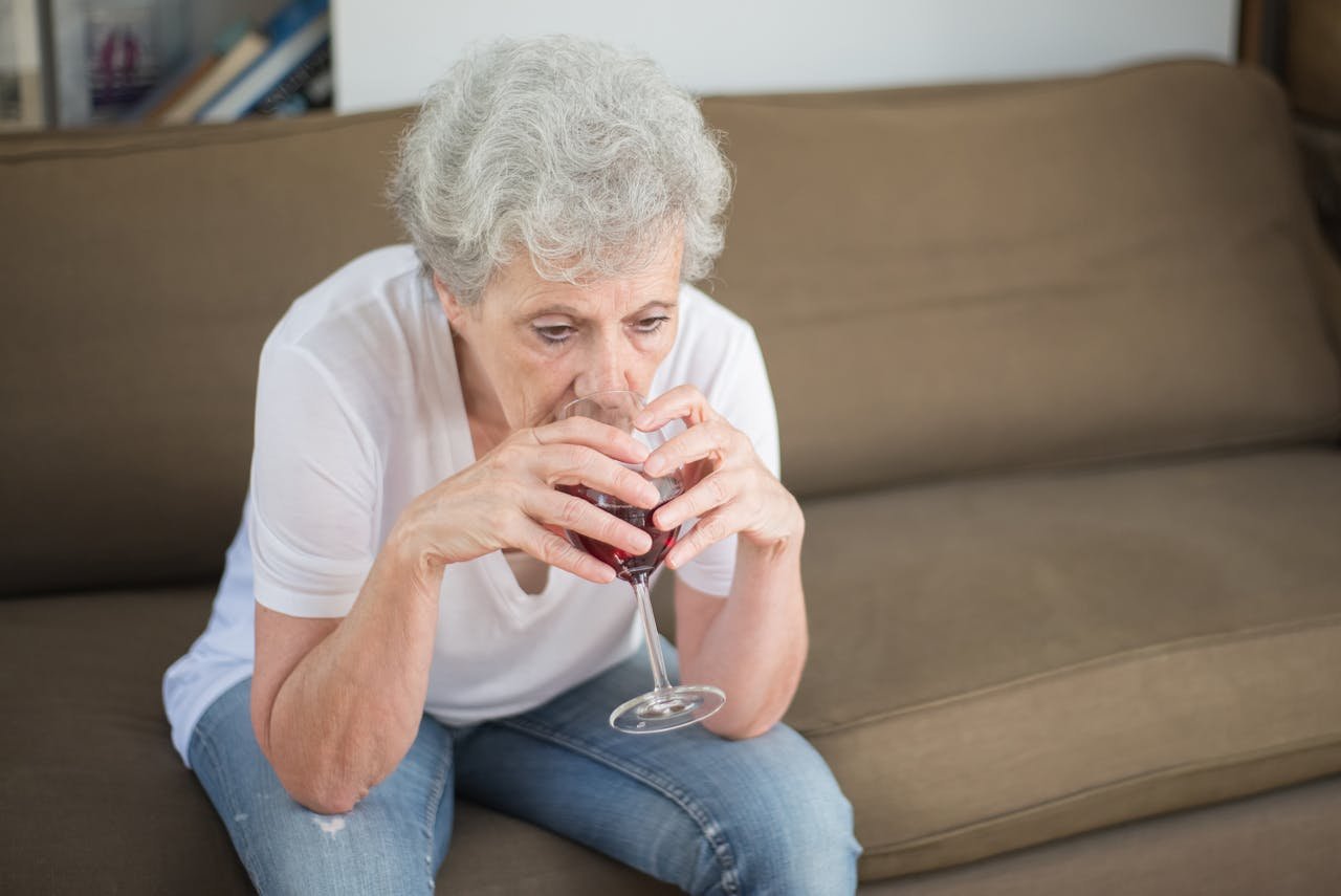 Older woman drinking wine on the couch.