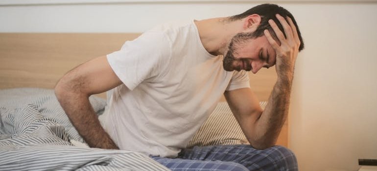 Man with a headache sitting on the edge of a bed.