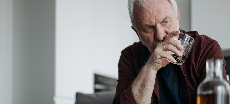 Older man drinking whiskey while suffering with grief and substance abuse.