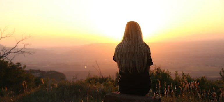 Woman sitting on the grass and looking at the sunset.