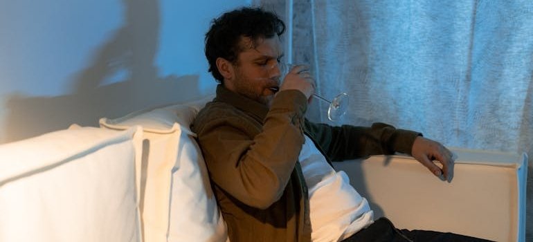 Man sitting on the couch and drinking a glass of wine while struggling with depression and addiction.