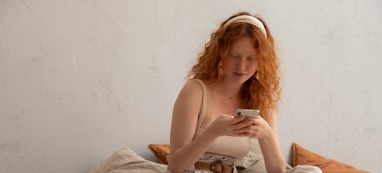 Woman sitting on the bed and logging her recovery progress into her phone.