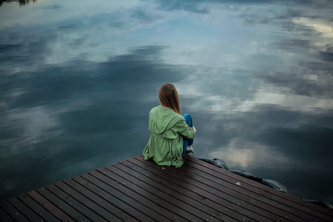 Woman sitting at a dock and looking out at the lake while struggling with seasonal affective disorder and addiction.