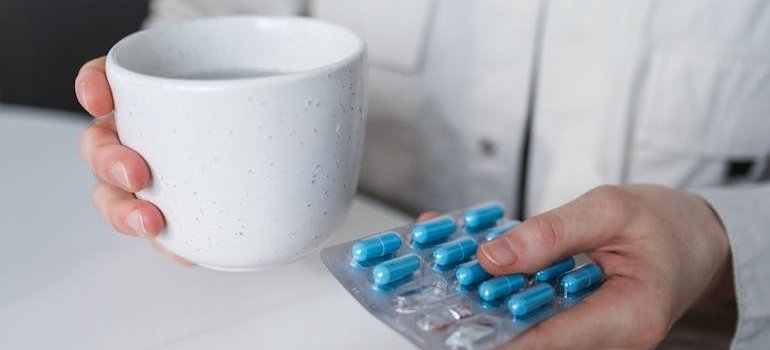 Person holding a blister of pills and a glass of water.