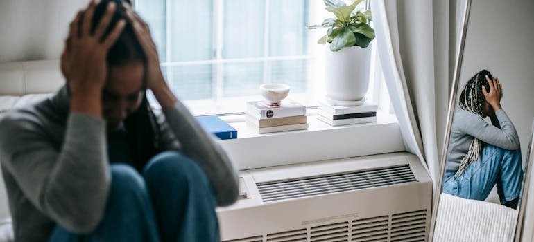 Woman sitting on the bed and holding her head.