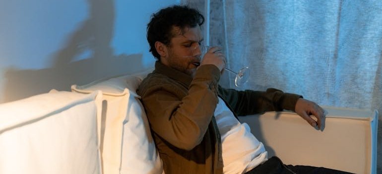 Man sitting on the couch drinking a glass of wine while thinking about his codependent relationship.