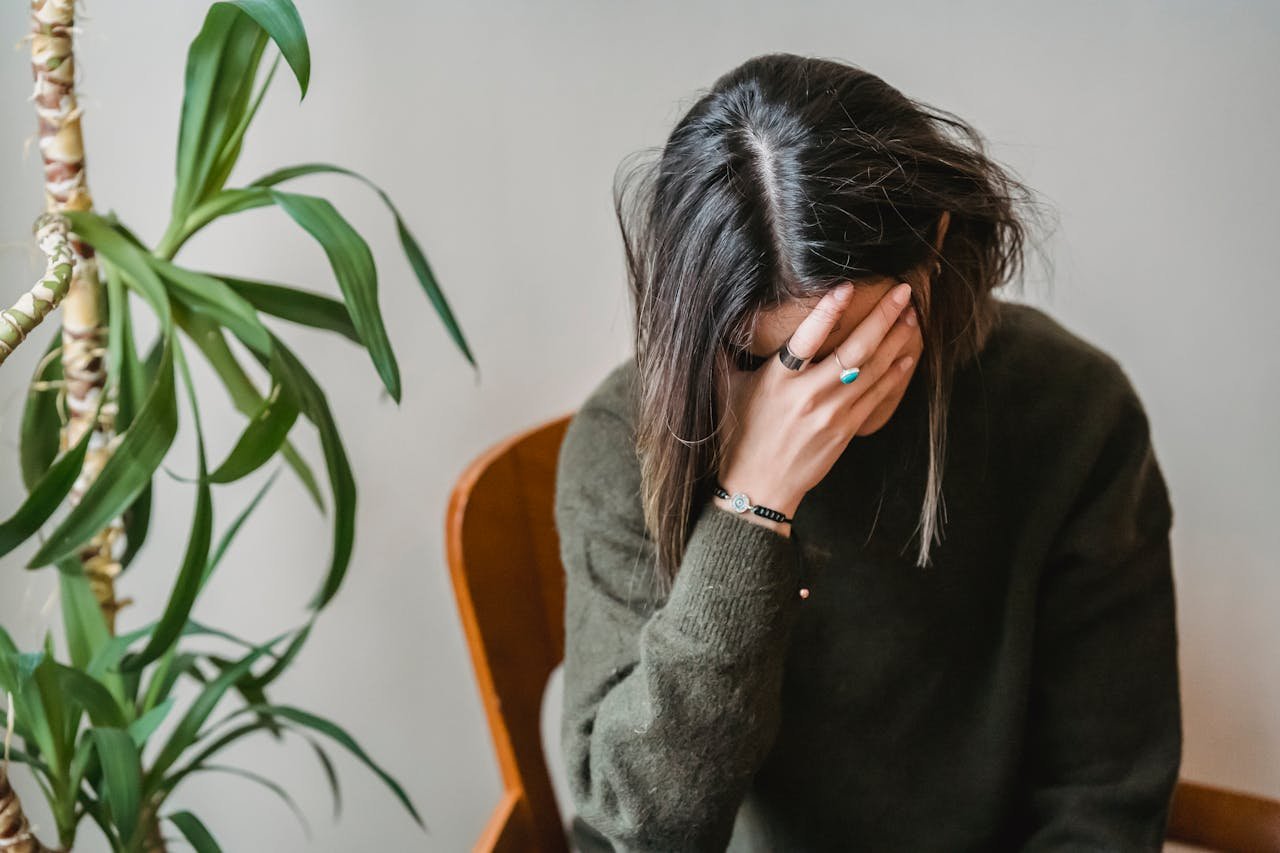 Woman sitting on a chair covering her face while worrying about how long does cannabis-induced anxiety last.