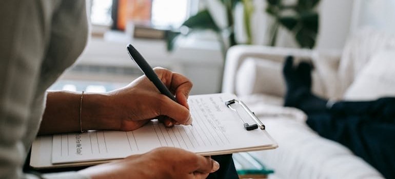 Therapist talking to a client while writing in a clipboard.