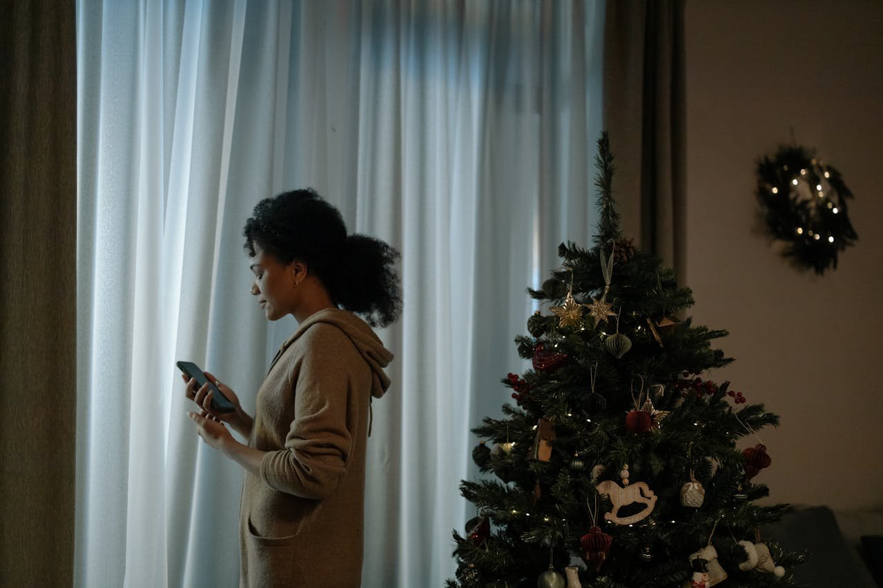 Woman standing next to a Christmas tree and looking out of the window.