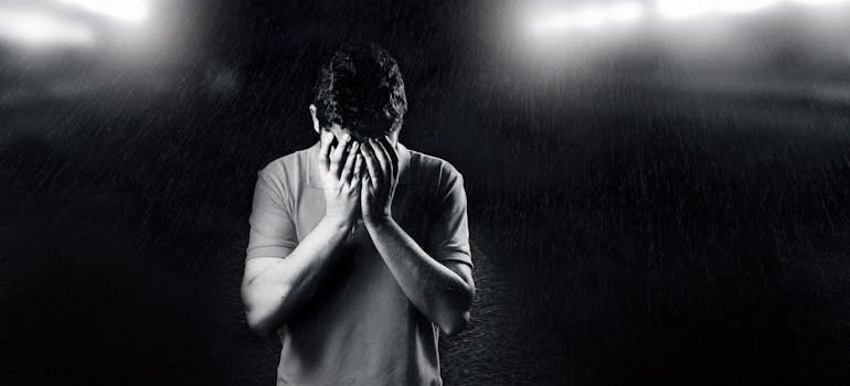 Black and white picture of a man covering his face with his hands.