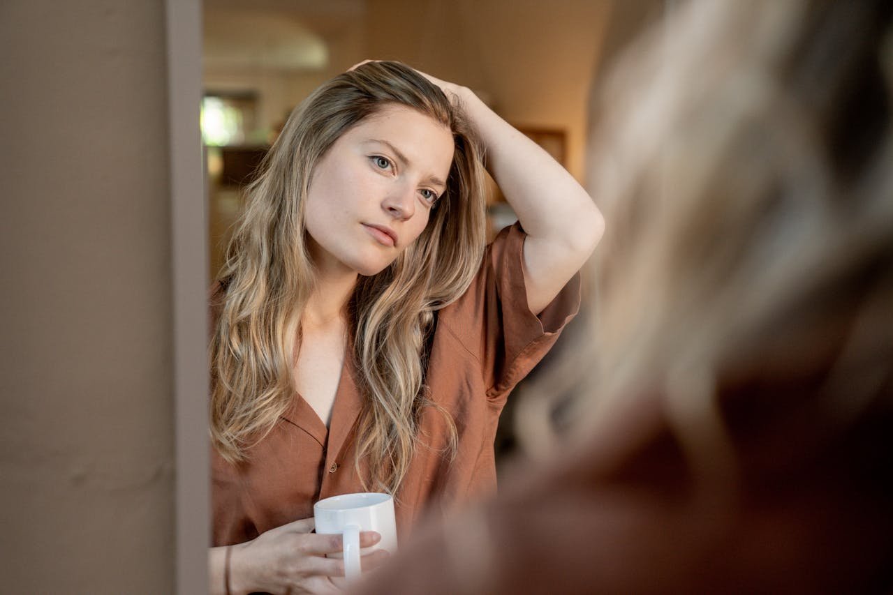 Woman holding a mug and looking at herself in the mirror.