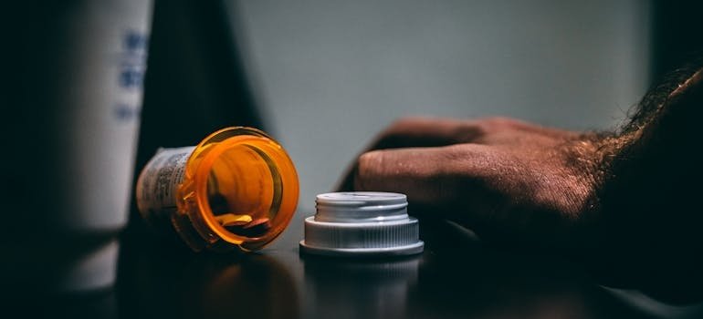 Man's hand next to an empty bottle of pills.