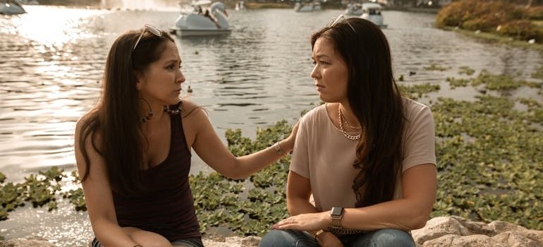 Two women sitting next to a lake and having a serious conversation.
