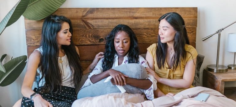 Two women comforting their friend while sitting in bed.