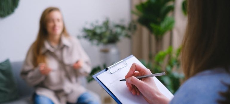 Therapist writing in a clipboard while talking to a patient.