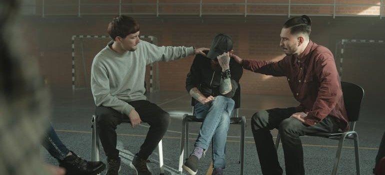 Two men comforting a man in a mental health support group.