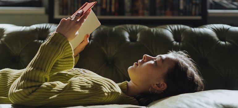 Woman lying down on a sofa and reading a book.