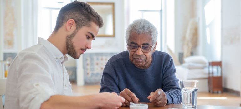 Younger man helping an elderly man with his pills.