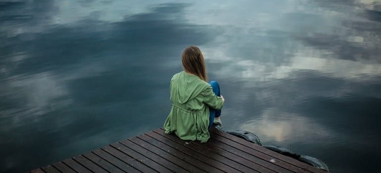 Depressed woman sitting on a dock near a body of water.