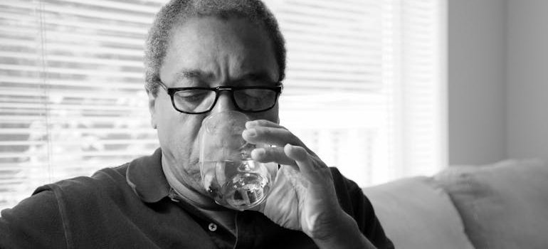 Elderly man drinking a glass of water after taking a pill.