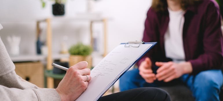 Therapist writing in a clipboard while talking to a patient.