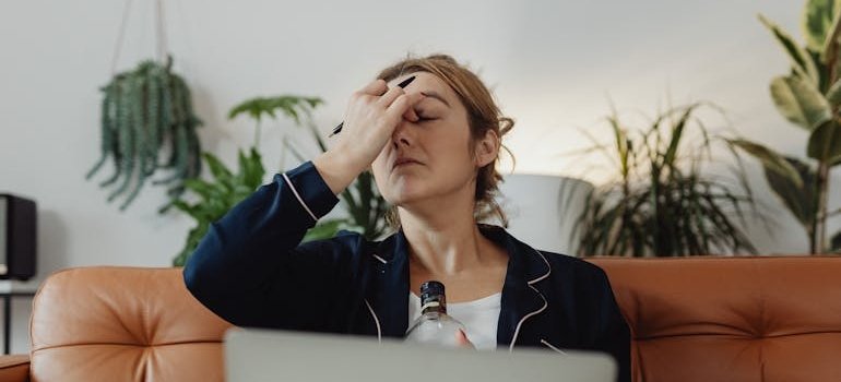 Woman pinching her nose in stress while holding a bottle of alcohol.