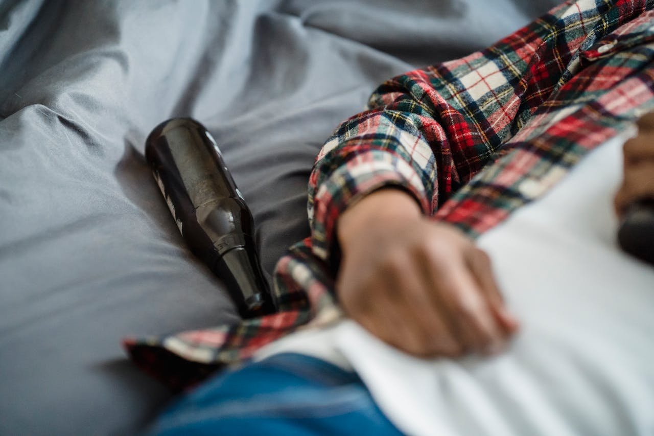 Empty beer bottle next to a man on the bed.