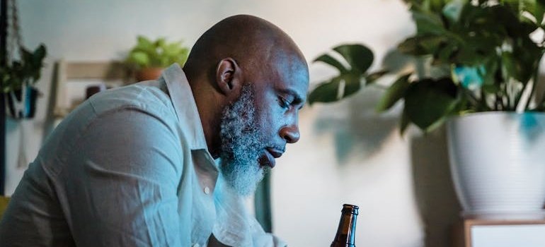 Sad man sitting on the couch and holding a bottle of beer.