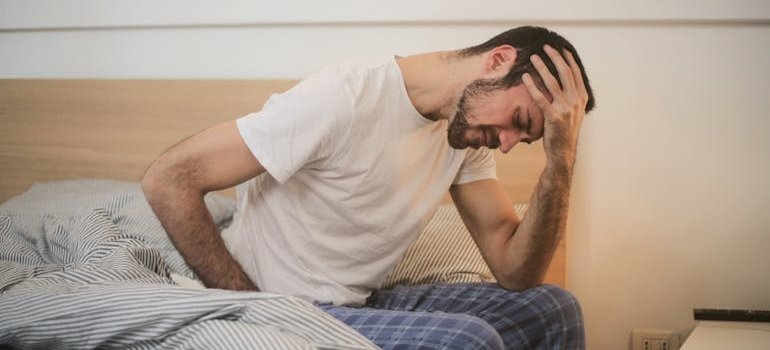 Man sitting on the bed while having a headache.