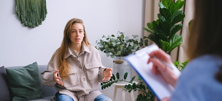 Doctor writing in a clipboard while her patient describes her medical history.